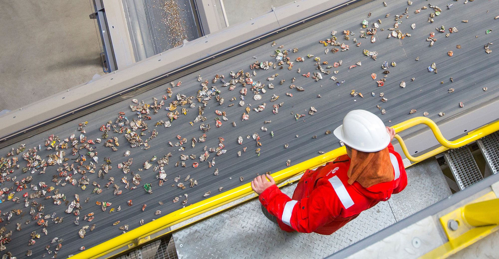 Worker observing conveyor belt with cans destined for recycling